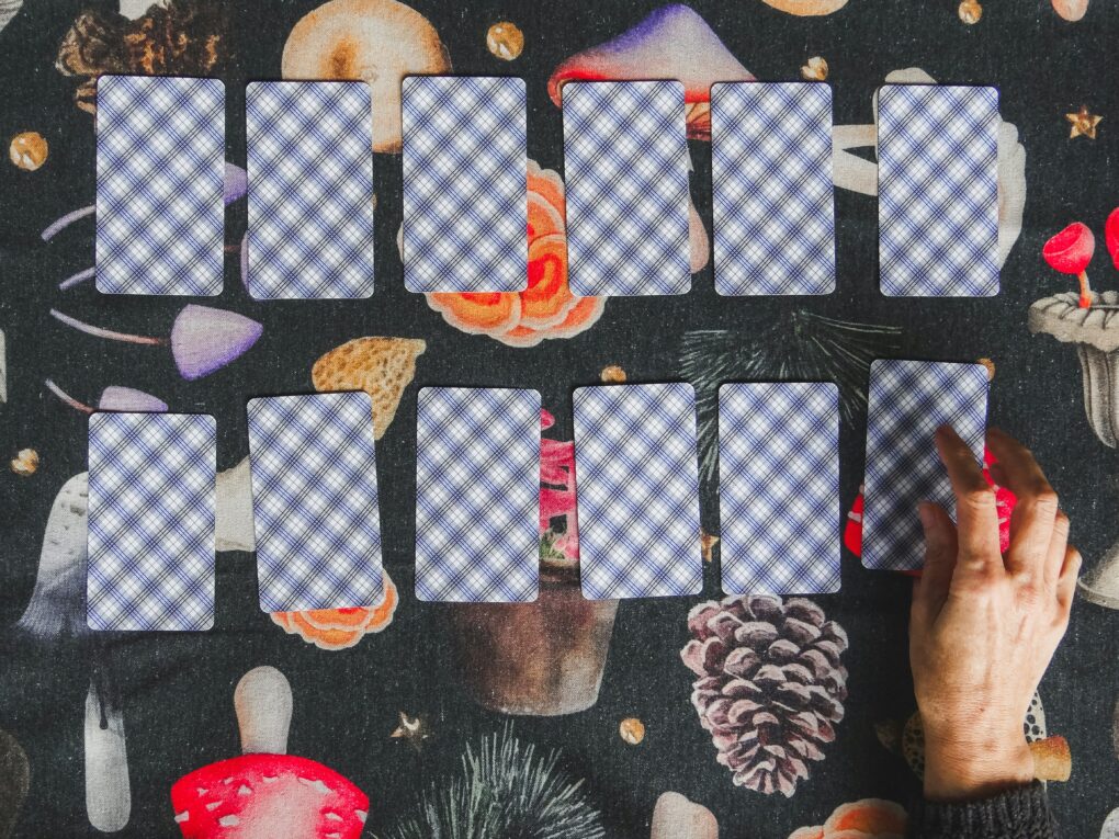 A hand lays out tarot cards upon a tablecloth covered in pictures of mushrooms and pinecones