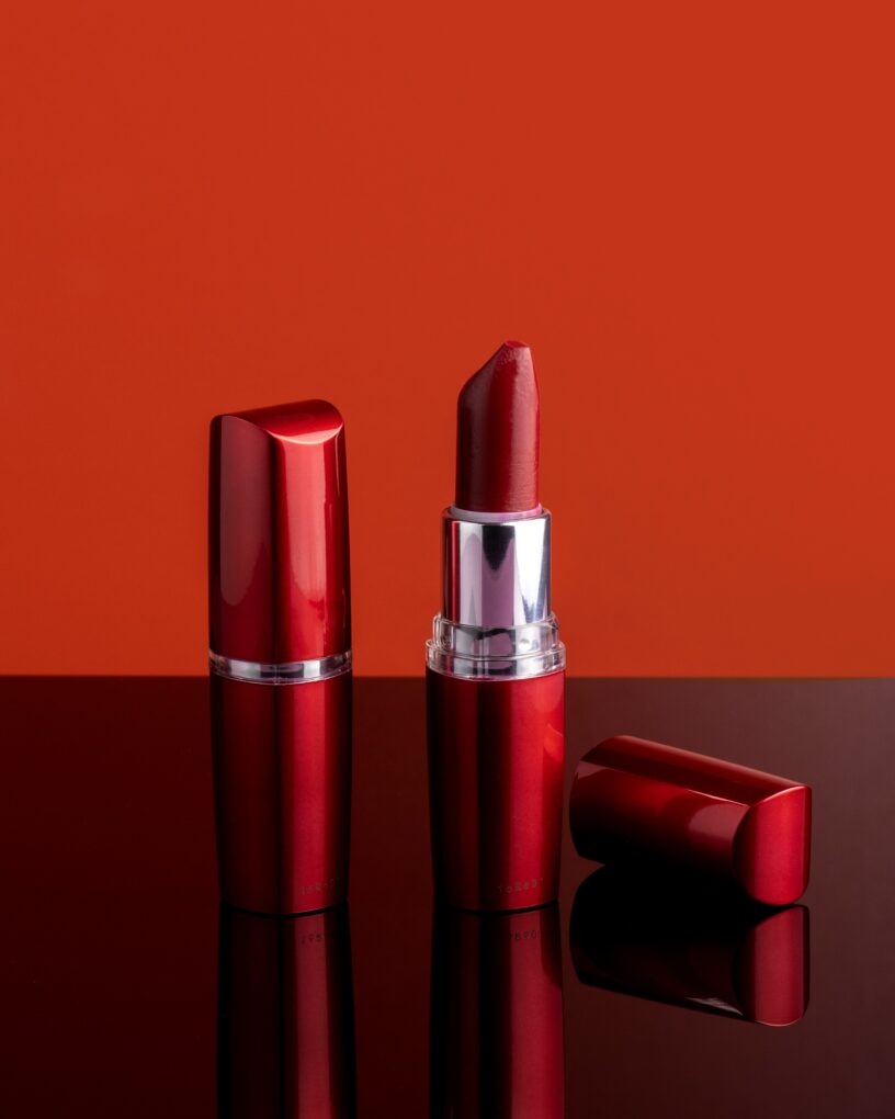 Two tubes of red lipstick before a red background. One lipstick has its cap removed.