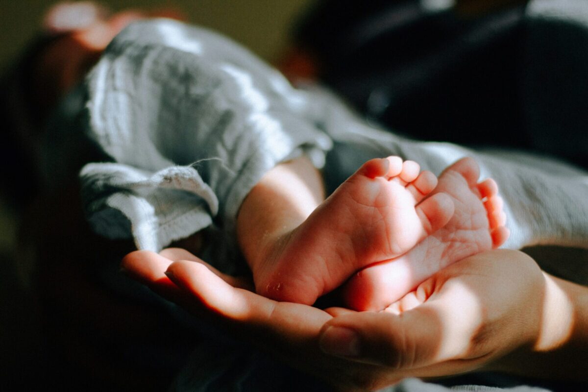 A close-up image of a parent holding a baby. The baby's little feet resting upon the parent's hand are the focus of the image.