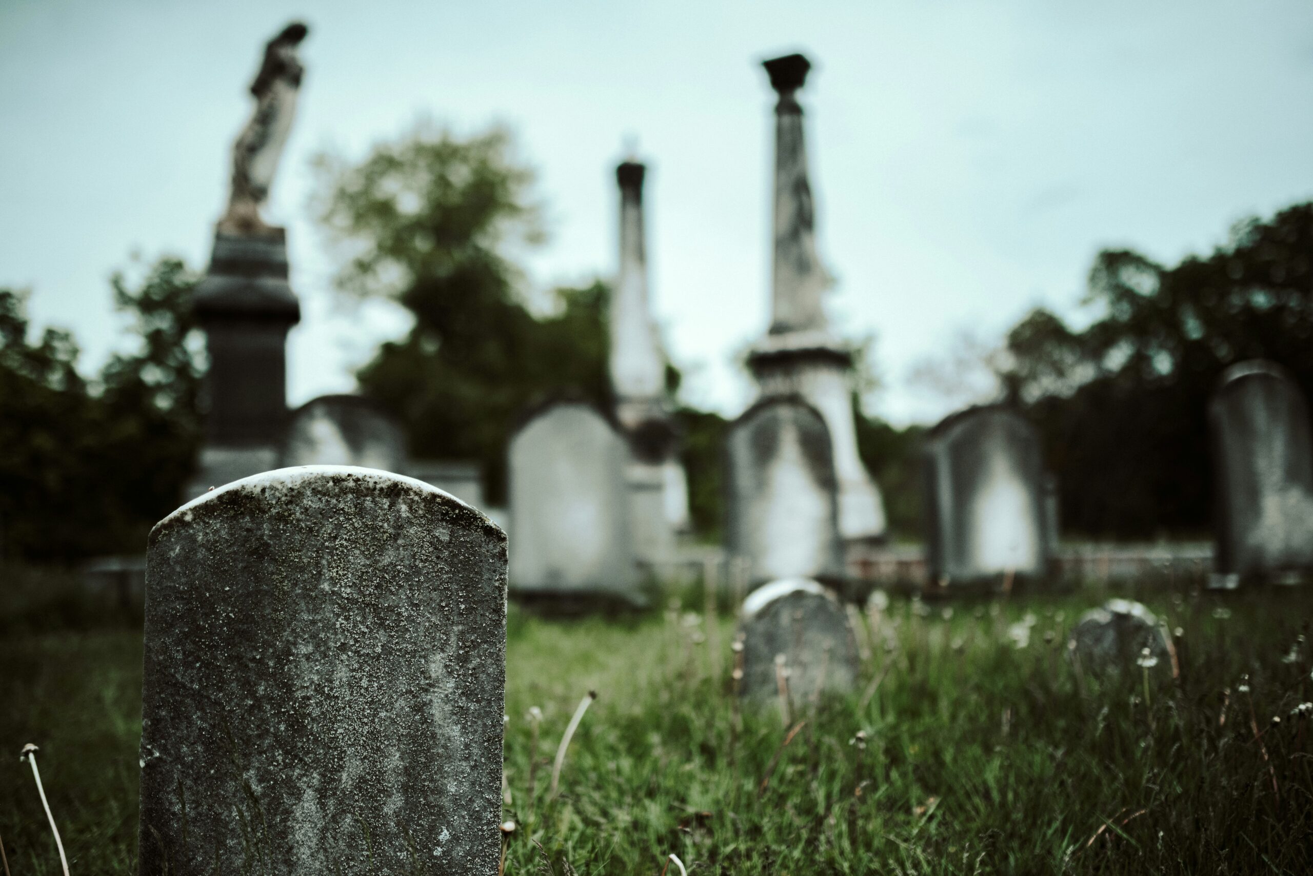 A concrete tombstone in a cemetery. Other graves are depicted in the background but are out of focus.
