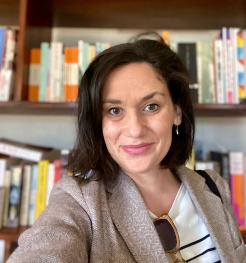 A photograph of Dr Bianca Denny in front of a bookcase. She has a medium-length brunette bob and is wearing a stone-coloured blazer with a white shirt.