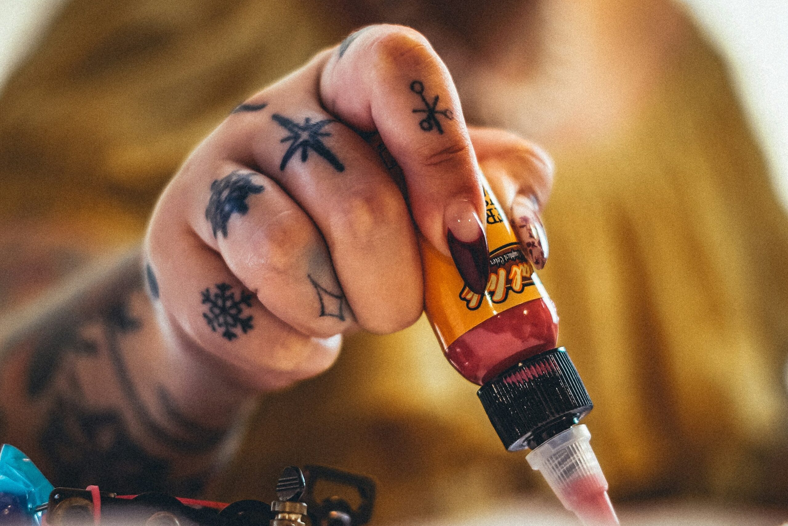 The hand of a tattoo artist holds a tube of red ink.
