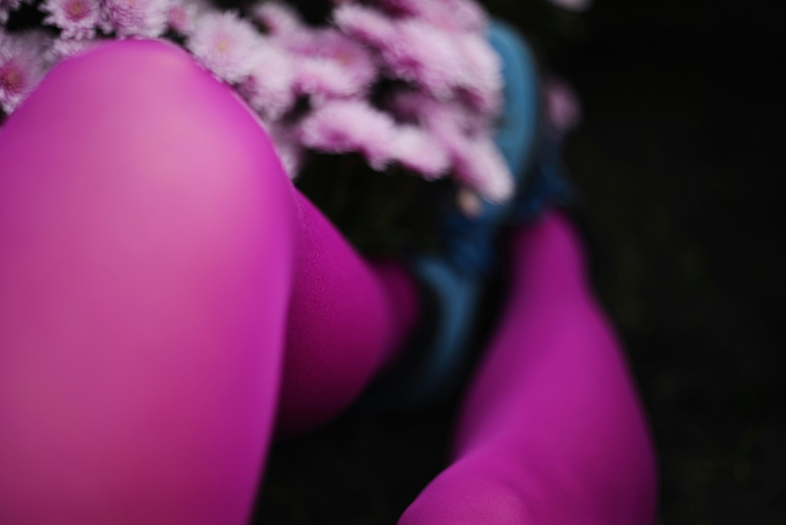 Purple-stockinged legs and a blue shoe are in focus against some blurred flowers