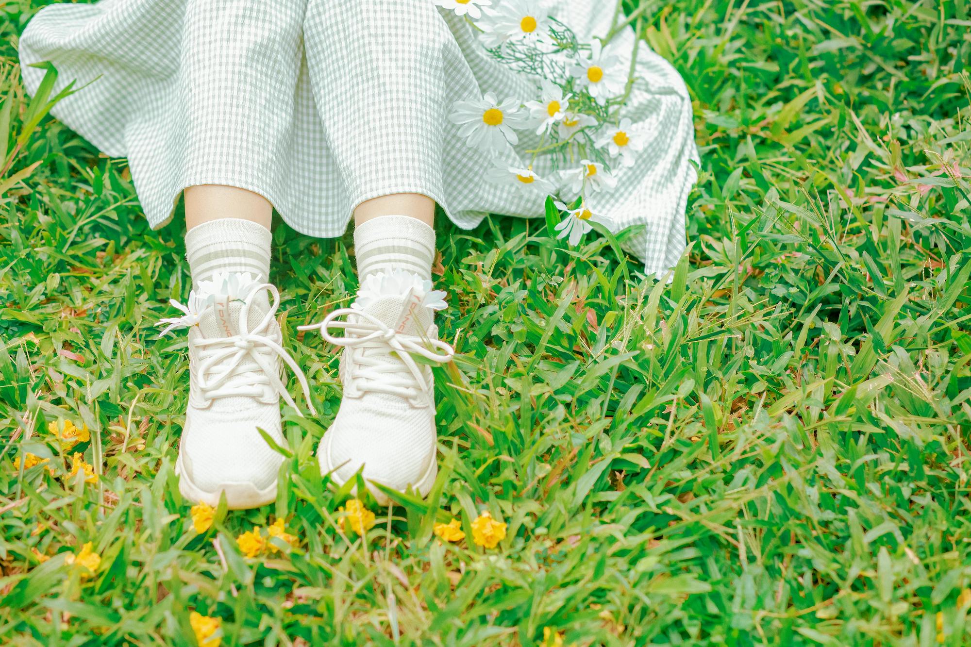A person is seated on the grass wearing sneakers and a gingham dress