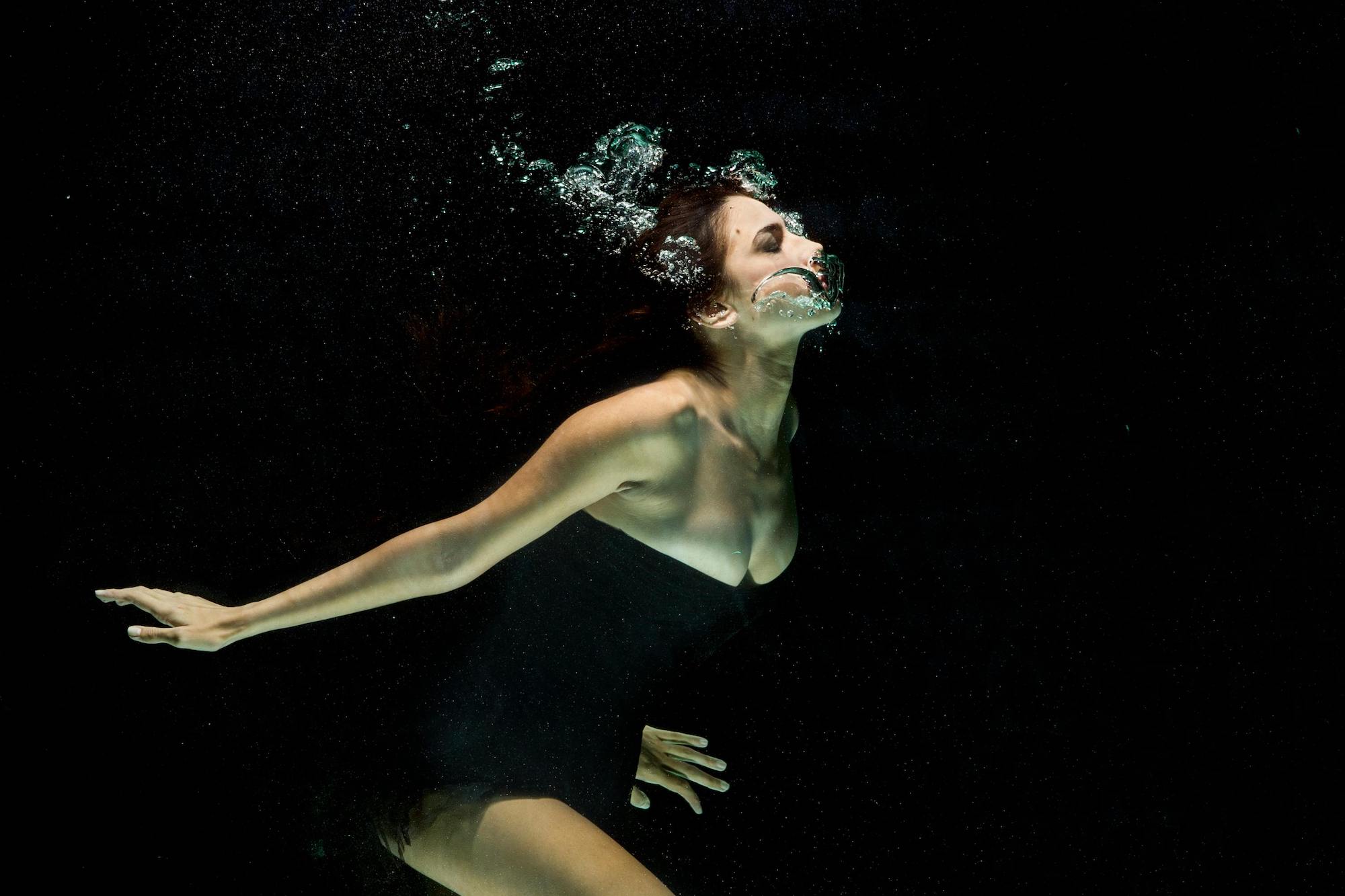 A person in black is submerged in water, exhaling bubbles.