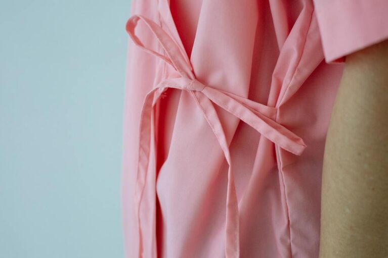 a person stands wearing a pink hospital gown tied at the front