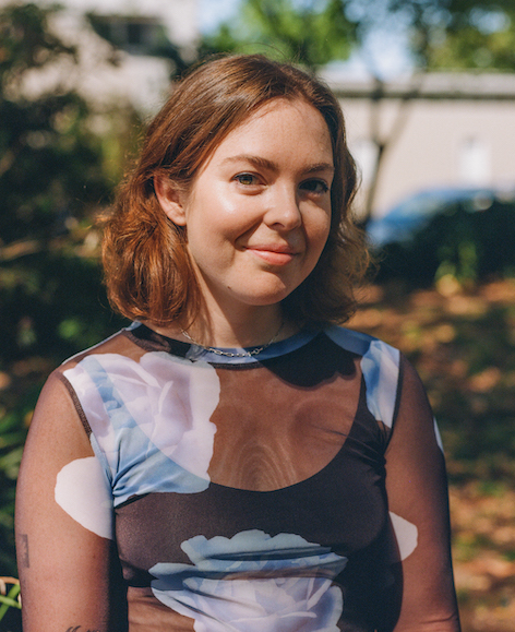 A portrait photograph of Tess. Tess wearing an outfit with a floral print and smiling at the camera.